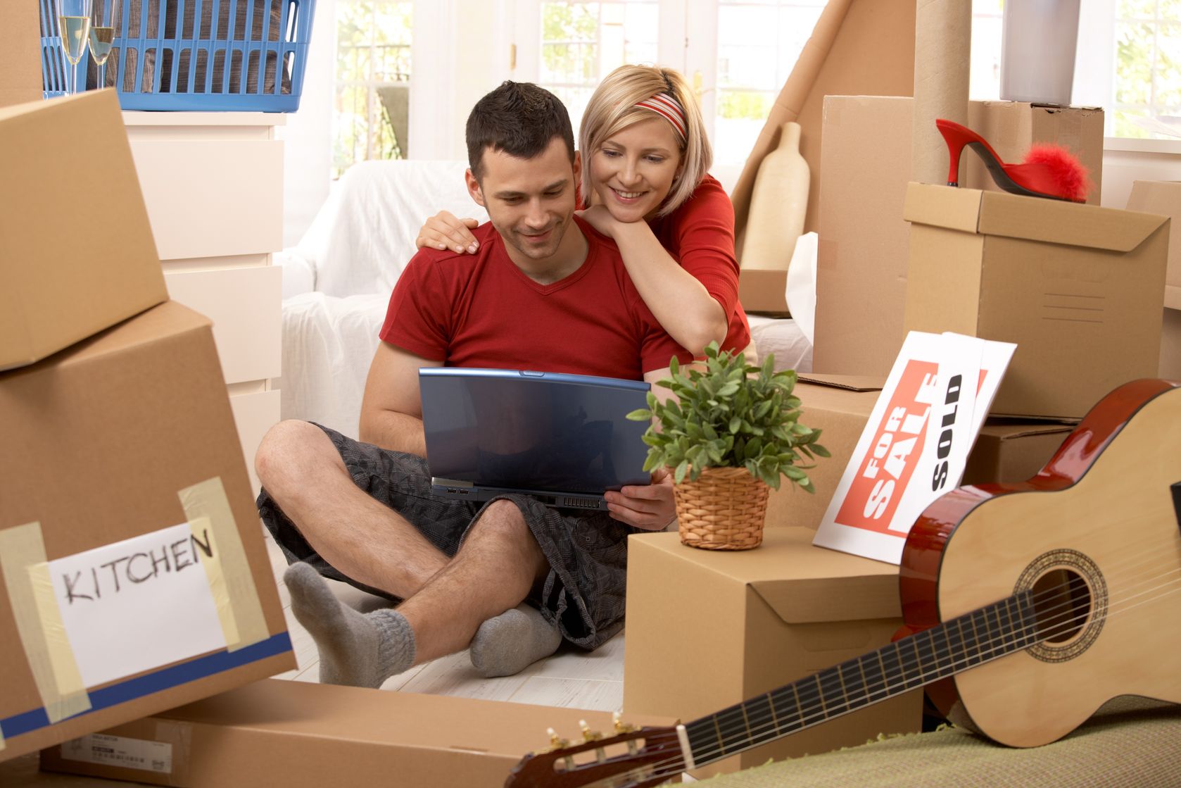 Man and Woman surrounded by moving boxes and looking at laptop